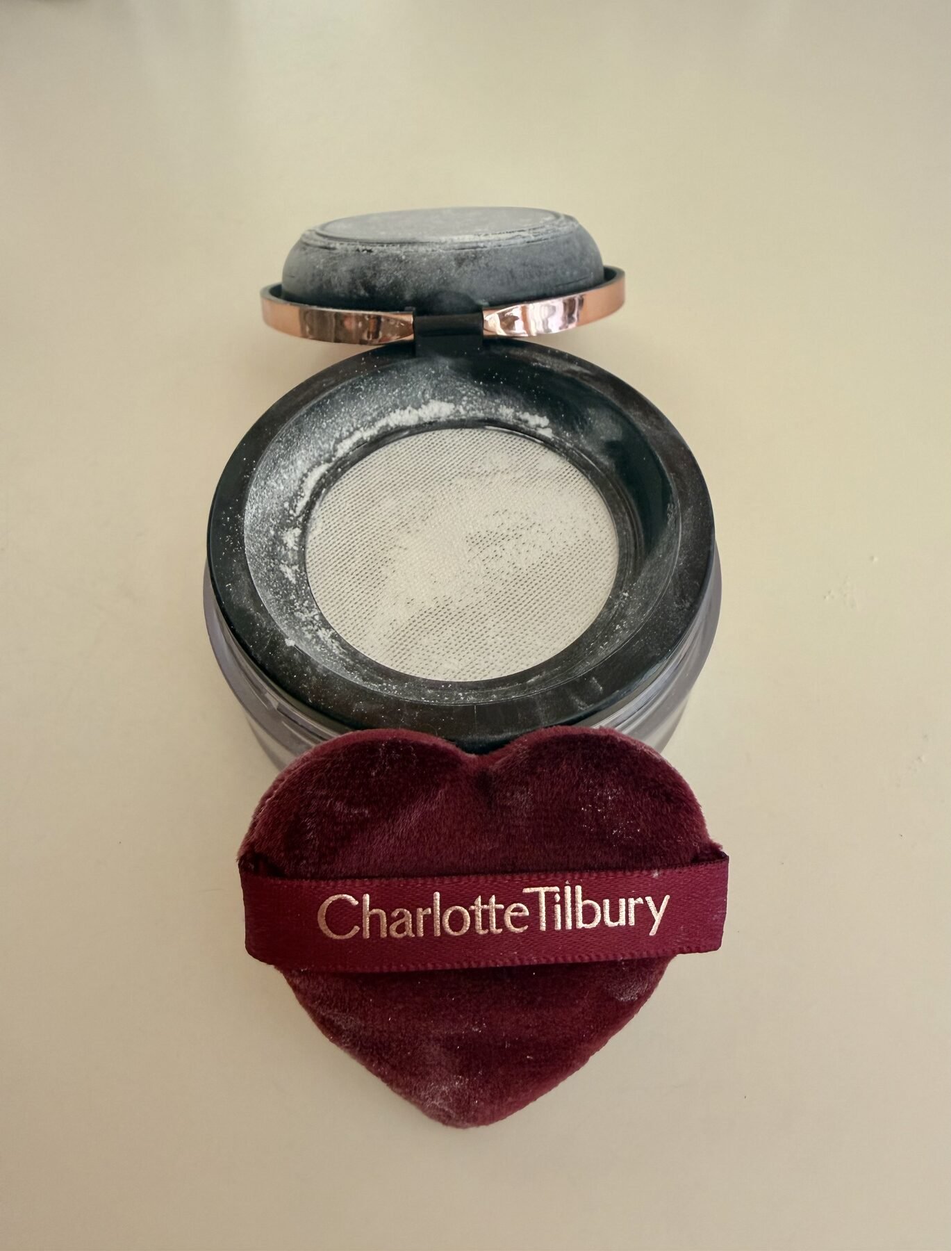 Open jar of Charlotte Tilbury loose setting powder with its heart-shaped velvet puff resting beside it.