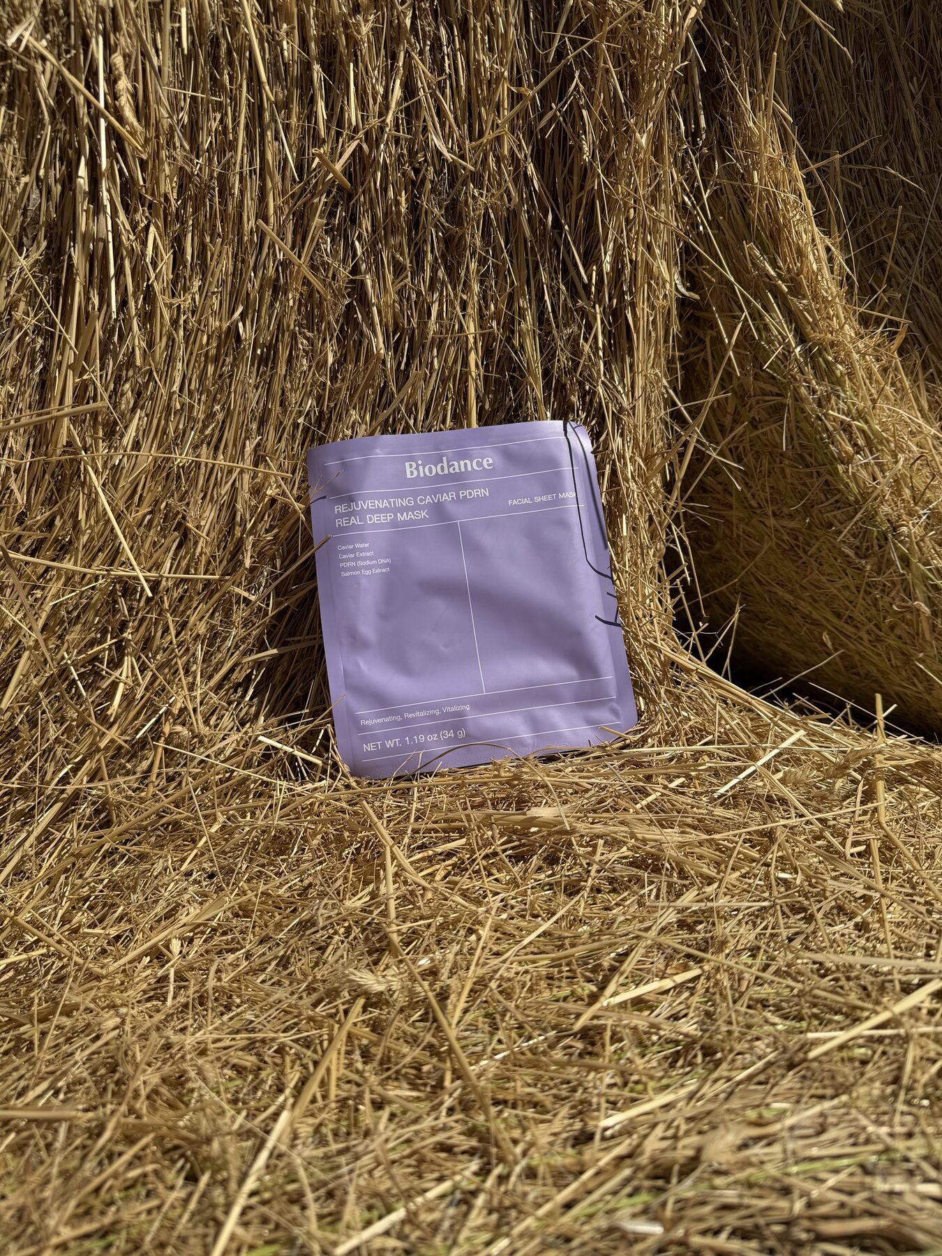 Purple Biodance Caviar PDRN sheet mask packet leaning against a straw hay bale.