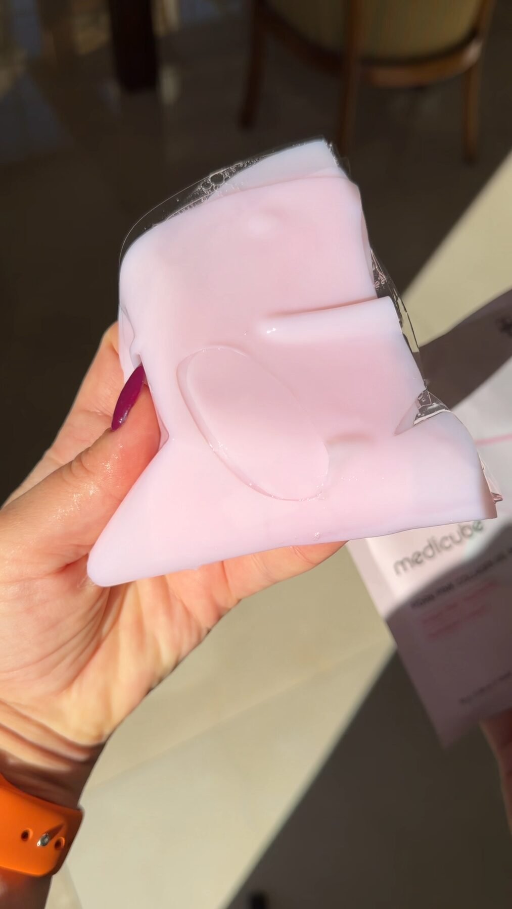 Hand holding a pink hydrogel sheet mask over its Medicube packaging box.