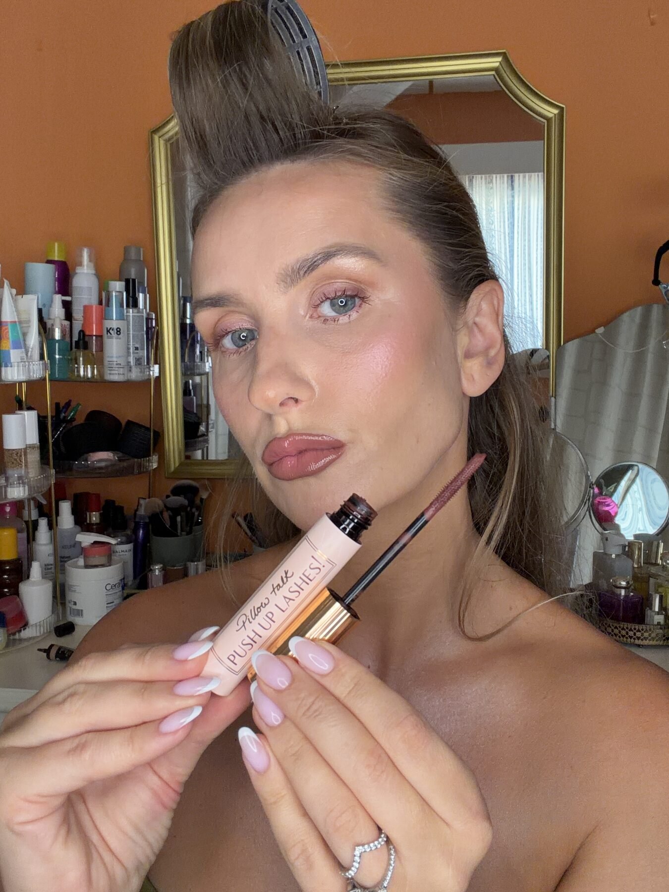 Woman holds up Charlotte Tilbury Pillow Talk Push Up Lashes mascara wand near her face at a vanity.