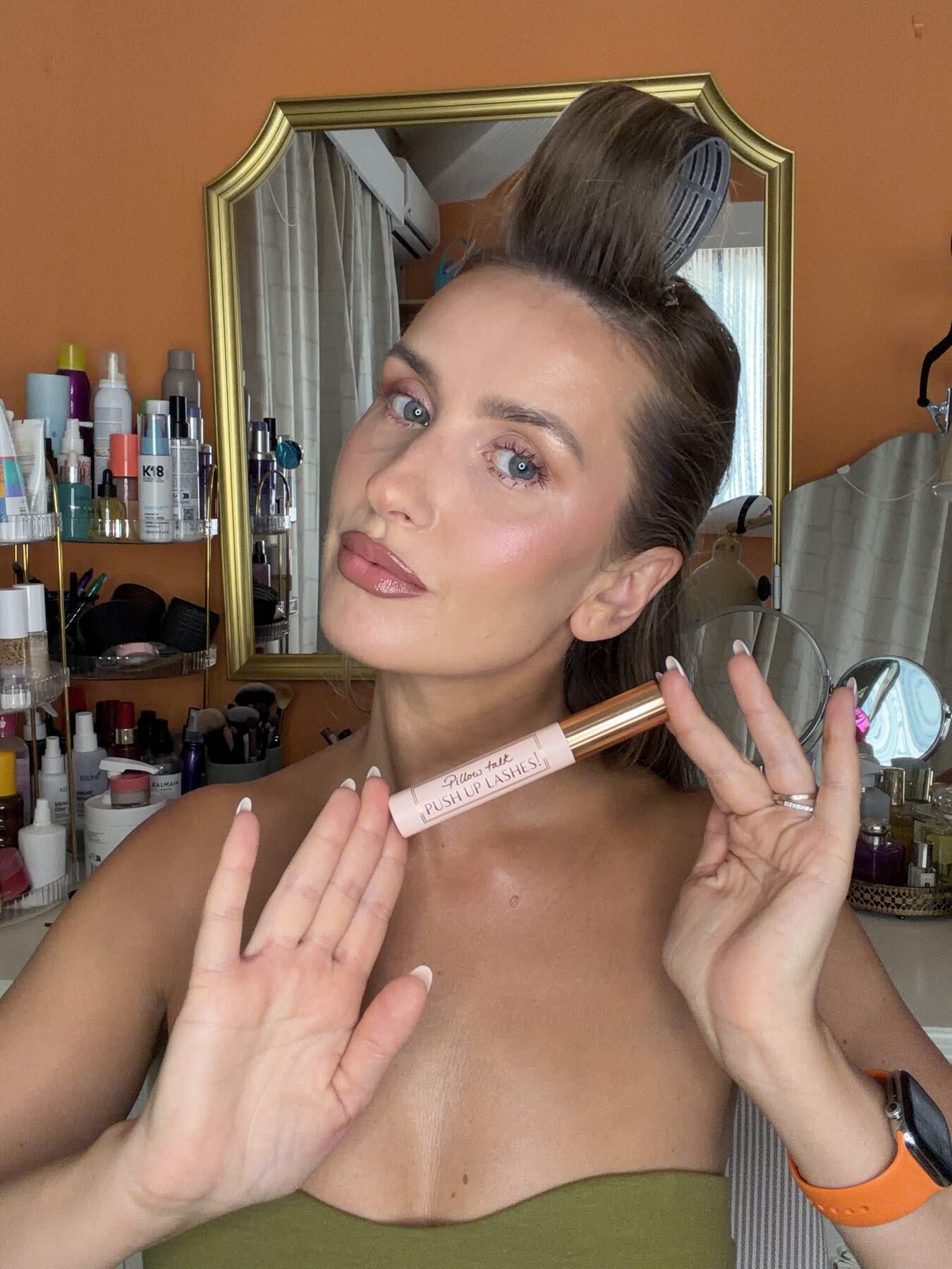 Woman with hair rollers holds up Charlotte Tilbury Pillow Talk Push Up Lashes mascara at makeup vanity.