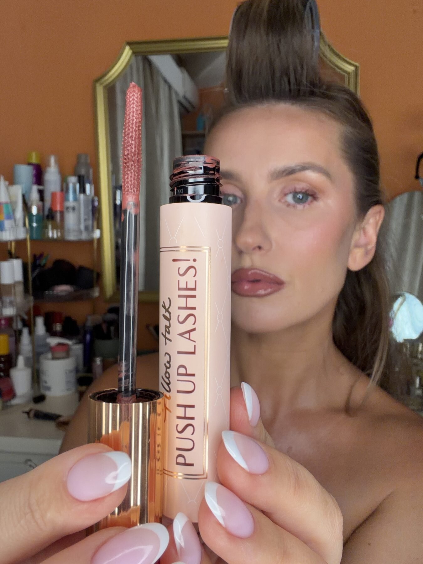 Woman with french-tip nails holds up an open Charlotte Tilbury "Push Up Lashes!" mascara wand near her face.