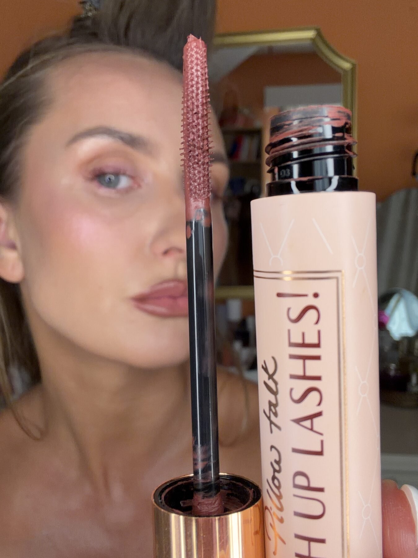 Woman holds up a mascara wand and its Pillow Talk Push Up Lashes tube near her face.