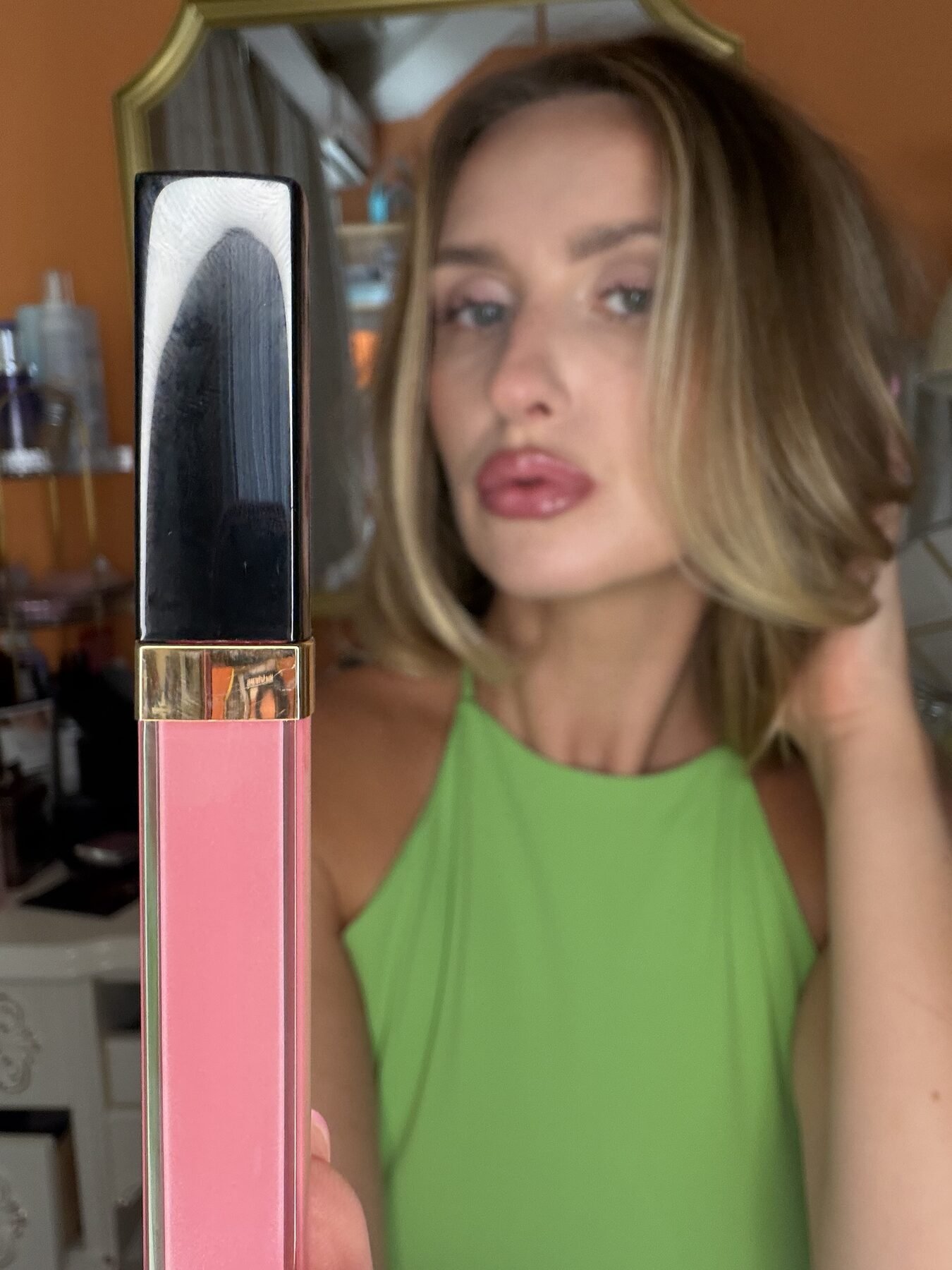 Woman with glossy pink lips holds up a Chanel lip gloss tube in a mirror selfie.