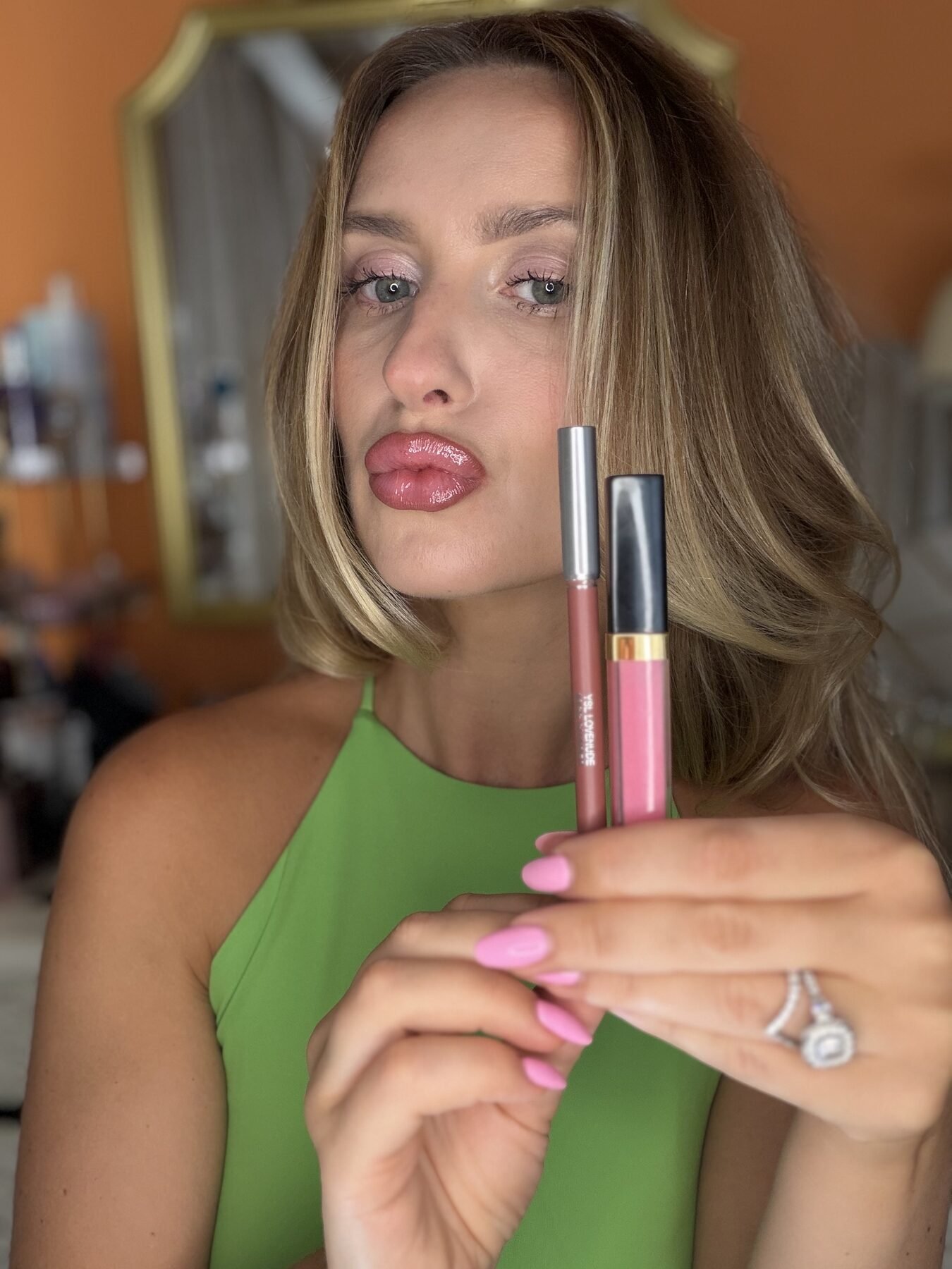 Woman with glossy pink lips holds up a lip liner and Chanel gloss tube for comparison.